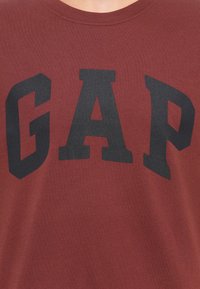 T-shirt med rund halsudskæring i mørkerød med store fede sorte bogstaver, der staver GAP over brystet.