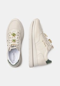 Sneakers in pelle beige con suola bianca spessa, accenti decorativi verdi e dorati sui lacci e una finitura liscia e lucida.