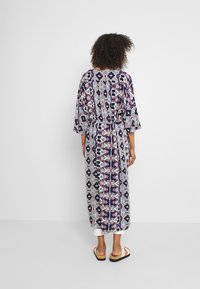 Langes, gemustertes Kleid mit kurzen, weiten Ärmeln. Der Stoff zeigt geometrische Designs in Marineblau, Pink und Weiß. Die Taille hat einen elastischen Bund und bietet eine entspannte Passform.