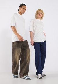 White oversized T-shirts paired with loose-fit brown and navy denim jeans. Casual footwear featured in gray with blue accents.
