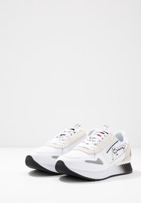 Białe sneakersy z beżowym zamszowym panelem, czarną gumową podeszwą i szarymi akcentami. Posiadają białe sznurówki i logo z boku.