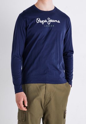 Osoba ubrana w granatową koszulę z długim rękawem z napisem "Pepe Jeans London", w połączeniu z oliwkowozielonymi spodniami typu cargo.