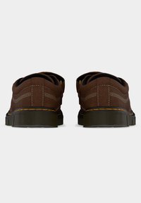 Ζευγάρι καφέ δερμάτινα παπούτσια με λευκή ραφή, μαύρο επενδεδυμένο κολάρο και παχιά μαύρη σόλα, από πίσω, σε απλό φόντο.