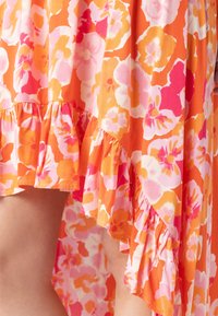 Bloemige jurk met een hoge-lage zoom, versierd met oranje, roze en gele bloemen op een lichtgewicht stof, benadrukt met een gerimpelde afwerking.