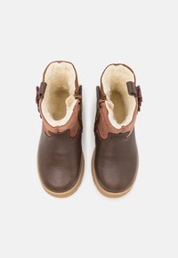 Bottines en cuir marron avec doublure en fausse fourrure tan, accents marron courbés, zips latéraux et semelle texturée marron.