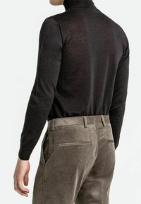 Sort turtleneck sweater med lange ærmer, parret med strukturerede, lysebrune corduroybukser med sidelommer og et bælte.