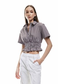 Camisa recortada a cuadros marrones y blancos con cuello y cintura fruncida, combinada con pantalones blancos de cintura alta. Textura suave, cierre de botones.