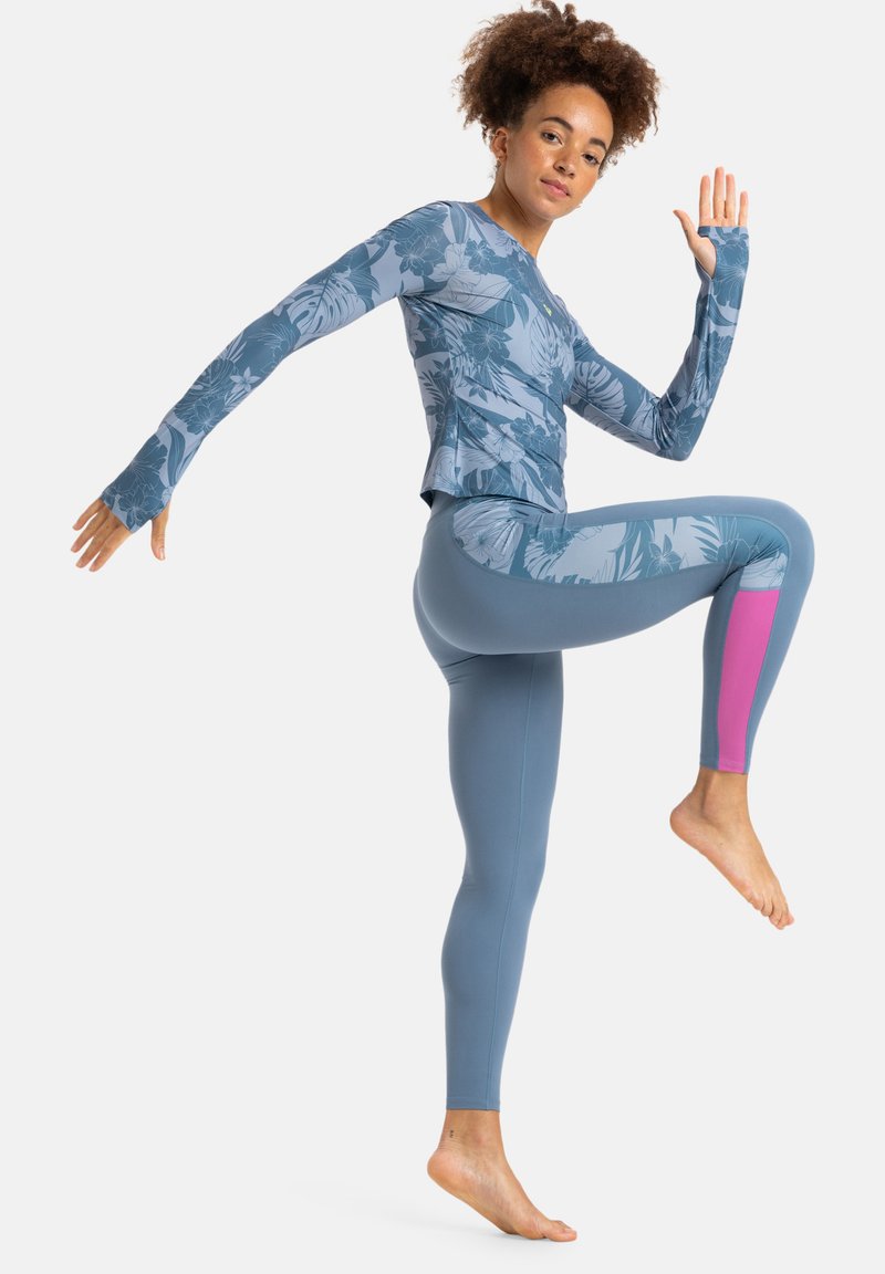 Langarm sporttop en leggings in lichtblauw met tropisch print. De leggings hebben een roze accent aan de rechterkant. Soepele textuur, rekbare pasvorm.