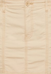 Beige bomullskjol med knäppning och synliga sömmar, med rak siluett och en lätt struktur i tyget.