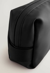 Sort kosmetikpose med en glat, mat finish, der har en robust lynlås og et tekstureret bånd omkring bunden for nem håndtering.