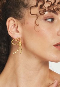 Zlaté kovové náušnice v tvare mašle, so špirálovými očkami a centrálnym zapínaním. Hladký povrch a lesklý finiš.