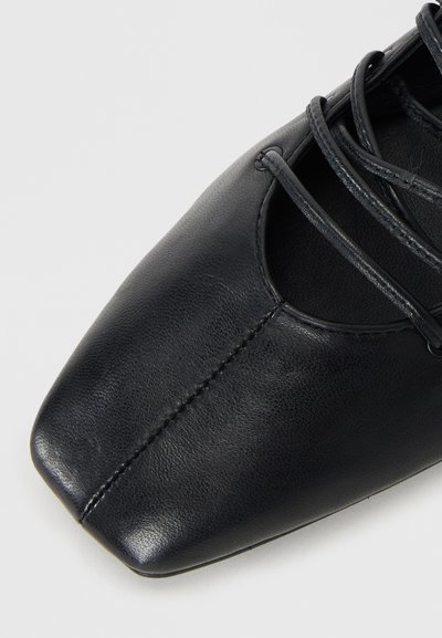 Chaussure en cuir noir avec un bout carré, dotée de lacets et de découpes sur les côtés, texture lisse et couture contrastante.