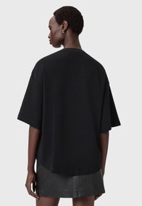 Camiseta negra de gran tamaño en tela suave con mangas cortas y dobladillo redondeado, mostrada por la parte trasera, combinada con una minifalda negra elegante.