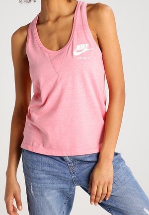Femme portant un débardeur rose Nike avec le texte « Just Do It », associé à un jean en denim bleu.