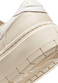 Beige lærersneakers med teksturert overdel, hvite detaljer og en tykk gummisåle. Merkelig mønster på yttersålen for bedre grep.
