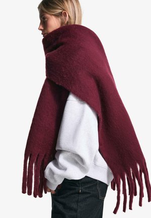 Bordeaux wollen sjaal met een zachte textuur, voorzien van lange franjes en een gedrapeerd ontwerp, gedragen over een grijze sweatshirt.