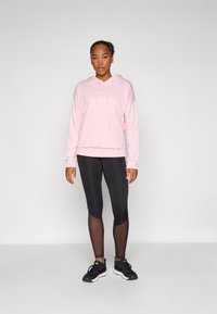 Rosa hoodie med känguruficka, svarta leggings med meshdetaljer och svarta träningsskor med vita sulor.
