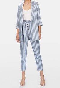 Pasiakowy niebiesko-biały żakiet z klapami, w zestawie z dopasowanymi spodniami typu tapered, które mają detale związywania i guzików. Przezroczysty, lekki materiał.