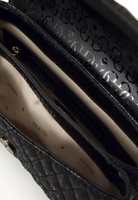 Schwarze gesteppte Handtasche mit geprägtem Logo-Design, ausgestattet mit mehreren Innenfächern und einem glatten Stofffutter. Goldene Hardware-Akzente.