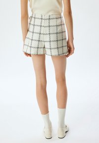 Witte tweed shorts met een zwart ruitpatroon, hoge taille en nauwkeurig toegepaste vorm. Gecombineerd met witte enkelkousen en beige schoenen.