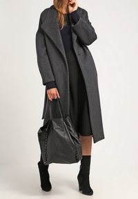 Abrigo de lana gris con solapas anchas, llevado sobre una blusa navy y una falda negra. Bolsa de cuero negro con detalles laterales, combinada con botas ankle.