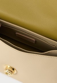 Smėlio spalvos odinė rankinės vidinė dalis su lygiu paviršiumi, žalia anga ir užtrauktuku užsegama kišenė. Matomi auksiniai metaliniai akcentai.