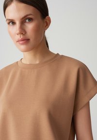 Felpa corta a maniche corte color marrone chiaro con scollatura a girocollo, caratterizzata da una superficie liscia e una vestibilità comoda. Dettagli di cucitura minimali arricchiscono il design.