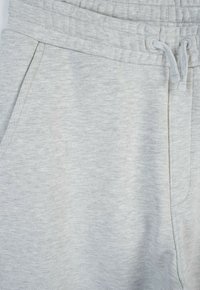 Jasnoszare dresy wykonane z miękkiego, teksturowanego materiału, z elastycznym pasem, sznurkiem i bocznymi kieszeniami.