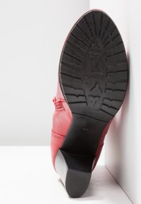 Bottine en cuir rouge avec semelle en caoutchouc noire et talon carré, motif de la semelle visible, taille 37 indiquée sur la semelle.