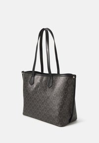 Saco tote cinza com padrão, apresentando alças escuras, um material texturizado e um design de logotipo geométrico. Parte superior aberta com detalhes laterais.