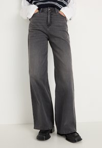 Posede grå denim jeans med høj talje, forlommer og en robust tekstur, parret med sorte platforniersko.