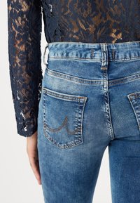 Jean en denim bleu délavé avec taille haute, couture visible et deux poches arrière avec des accents de fil contrastants.