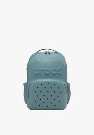 Lichtblauwe Crocs rugzak met een gestructureerde bovenkant, geperforeerde voorkant en gegraveerd "crocs" logo, weergegeven tegen een witte achtergrond.