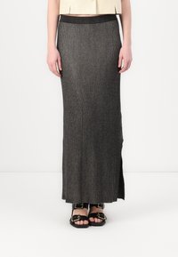 Lång, svart ribbad stickad kjol med en åtsittande midja och sida slits. Bärs med svarta sandaler som har detaljer i guld.