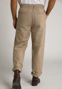 Pantalons beige à coupe décontractée avec une taille élastique, dotés de deux poches arrière et de poignets retroussés, associés à des bottes marron foncé.