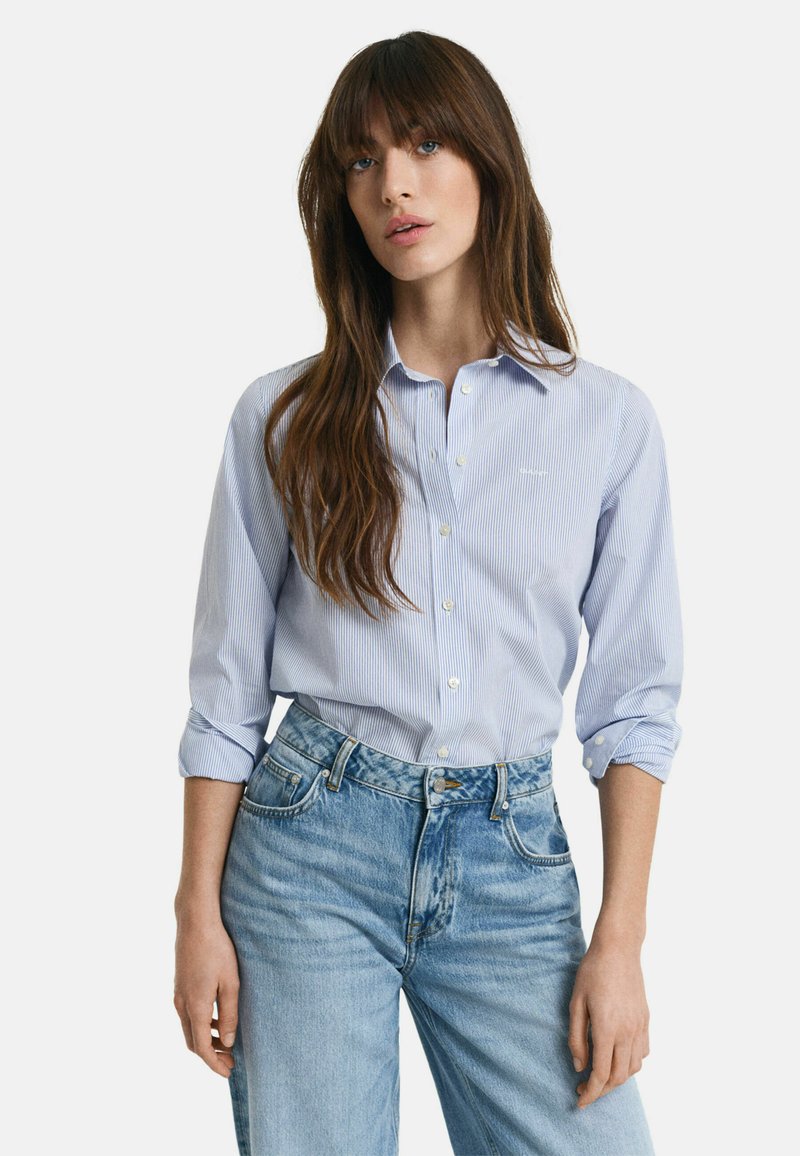 Camicia button-up a righe blu chiaro con maniche lunghe arrotolate ai polsini, abbinata a jeans in denim chiaro a vita alta.