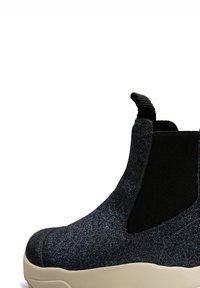 Botín negro con purpurina y paneles laterales elásticos, con un acabado texturizado. Presenta una suela sólida de color crema y una cinta en la parte trasera para tirar.
