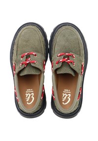 Zapatos de ante verde estilo mocasín con cordones rojos y blancos, punta redonda y suelas de goma negra. El interior tiene una etiqueta de plantilla marrón.