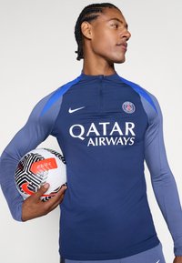 Dark blue long-sleeve shirt with blue accents, featuring "QATAR AIRWAYS" logo and Paris emblem, paired with a black and white patterned soccer ball.