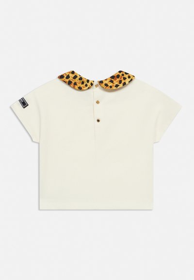 Chemise crème à manches courtes avec trois boutons devant et col Peter Pan imprimé léopard, avec une petite étiquette noire sur la manche gauche.