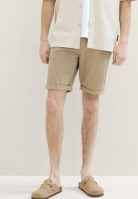 Pantaloni scurți din bumbac bej cu manșete răsucite, asociați cu o cămașă de culoare deschisă și pantofi slip-on din suede în nuanță de bej. Design simplu și casual.