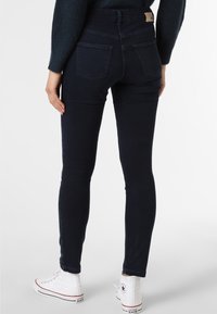 Persona vistiendo jeans ajustados azul oscuro, suéter navy y zapatillas Converse blancas de caña alta, mostrada de espaldas.