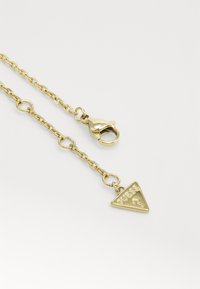Gouden ketting met driehoekige hanger. De hanger heeft het reliëf-logo "GUESS" en een vraagteken, met een karabijnsluiting.
