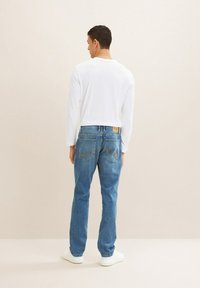 Modri jeans z sproš�čenim krojem, ravnimi hlačnicami in kontrastnim rumenim šivom, ter dolgom rokavu belega srajca in belimi supergami.
