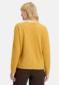 Żółty, puszysty sweter o luźnym kroju, z długimi rękawami i okrągłym dekoltem. Teksturowana powierzchnia i żeberkowane mankiety podkreślają jego design.