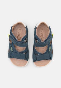 Navy blue sandals with suede upper, two adjustable straps, and beige leather lining. Features subtle green accents and robust sole.
