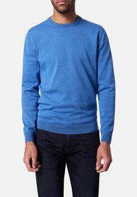 Blauer Langarmpullover, Rundhals, aus weichem Stoff, mit gerippten Bündchen und Saum, über dunklen Hosen getragen, glatte Textur.