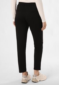 Pantalones elásticos negros con un diseño ajustado, que cuentan con dos bolsillos traseros y una pretina elástica, combinados con zapatillas color beige claro.