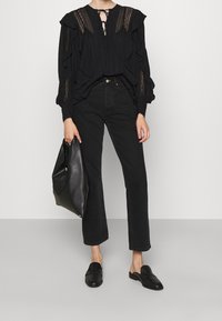 Blusa nera con texture, maniche a volant, dettagli in pizzo, abbinata a jeans neri a gamba dritta e mocassini neri piatti. Inclusa una borsa a tracolla nera.