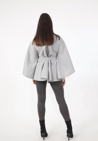 Lichtgrijze wikkeljas met wijde mouwen en een ceintuur, met een geplooid ontwerp aan de achterkant. Gecombineerd met aangesloten grijze broek en zwarte laarzen met hak.